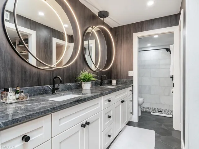 Bathroom featuring a tile shower, double vanity, a sink, and toilet