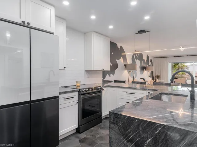 Kitchen featuring backsplash, a sink, freestanding refrigerator, white cabinetry, and electric stove