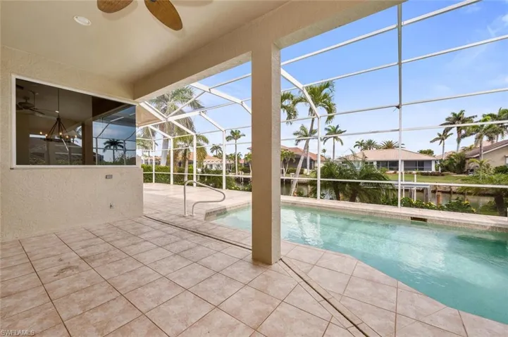 View of swimming pool with a patio area, a water view, ceiling fan, and glass enclosure