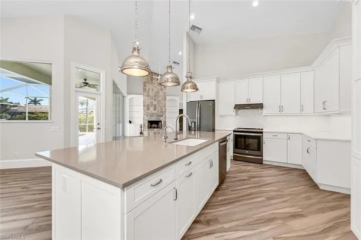 Kitchen featuring sink, white cabinetry, a center island with sink, appliances with stainless steel finishes, and a fireplace