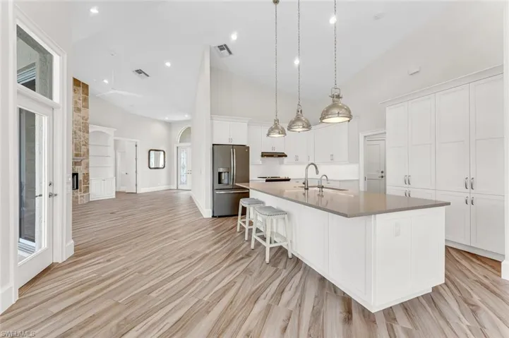 Kitchen featuring high vaulted ceiling, decorative light fixtures, white cabinetry, stainless steel refrigerator with ice dispenser, and a spacious island