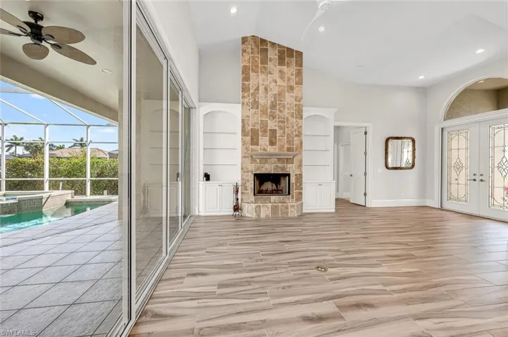 Unfurnished living room featuring built in shelves, french doors, a stone fireplace, high vaulted ceiling, and ceiling fan