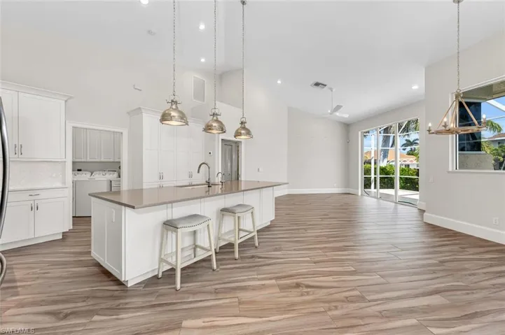 Kitchen featuring washer and dryer, high vaulted ceiling, decorative light fixtures, white cabinetry, and an island with sink