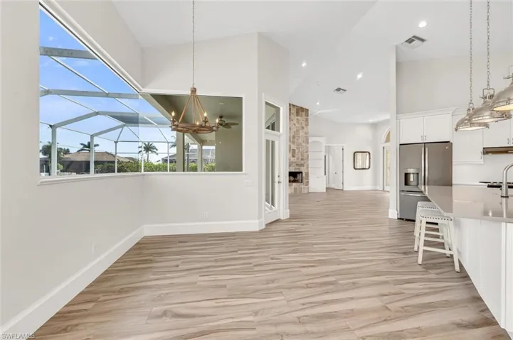 Unfurnished dining area featuring an inviting chandelier, a towering ceiling, light hardwood / wood-style flooring, and a large fireplace