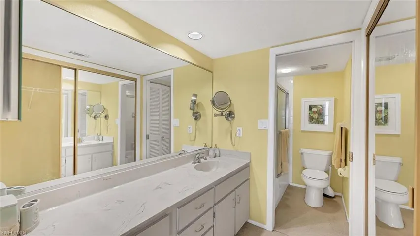 Bathroom featuring a closet, enclosed tub / shower combo, vanity, and light colored carpet