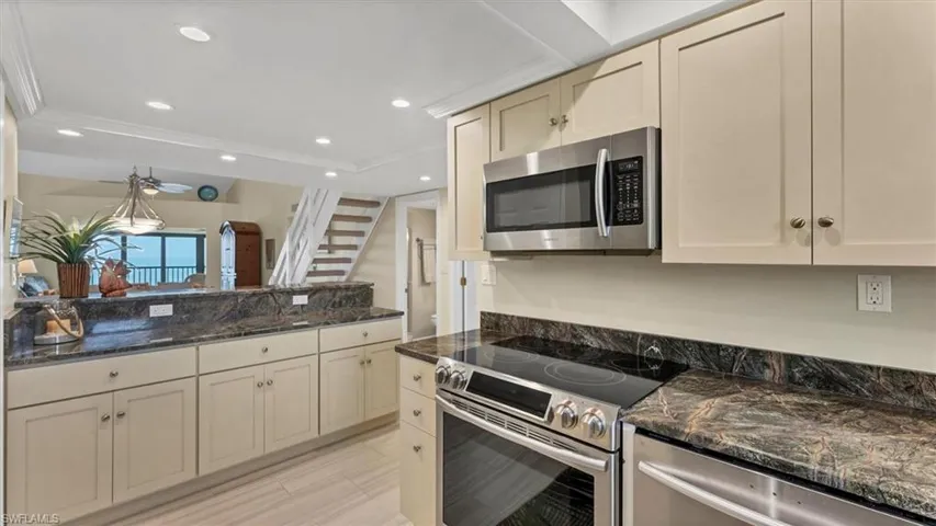 Kitchen with stainless steel appliances, dark stone countertops, recessed lighting, cream cabinets, and ornamental molding