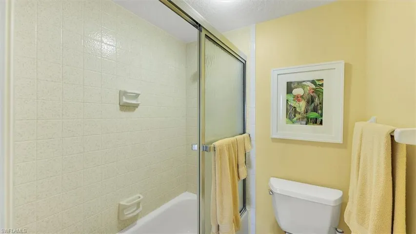 Bathroom featuring combined bath / shower with glass door and toilet