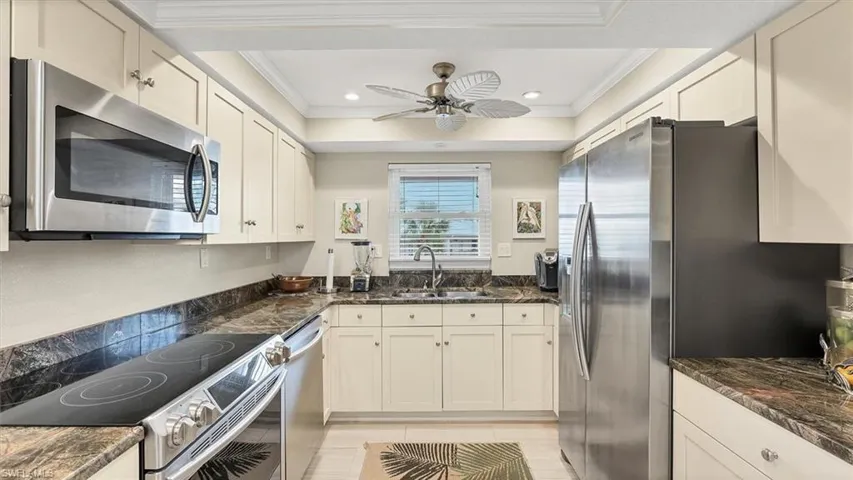 Kitchen featuring appliances with stainless steel finishes, dark stone countertops, a ceiling fan, ornamental molding, and recessed lighting
