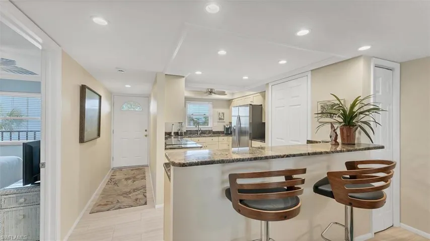 Kitchen with a breakfast bar, a peninsula, dark stone counters, stainless steel refrigerator with ice dispenser, and recessed lighting