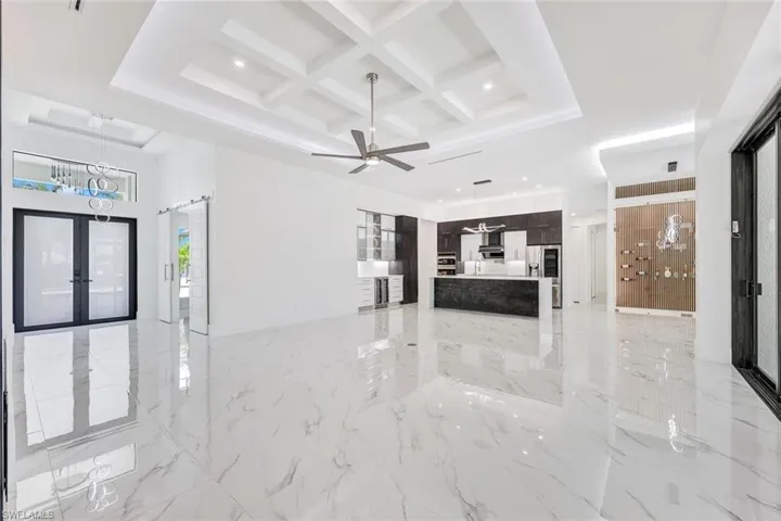 Unfurnished living room featuring ceiling fan, coffered ceiling, french doors, beamed ceiling, and light tile patterned flooring