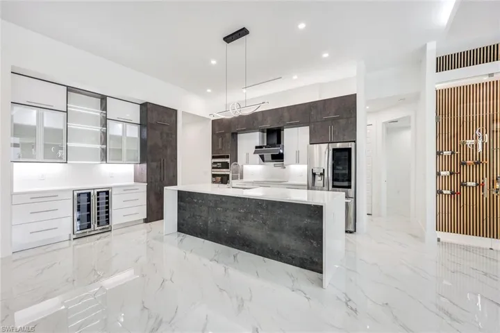 Kitchen featuring appliances with stainless steel finishes, wall chimney exhaust hood, dark brown cabinets, an island with sink, and light tile patterned floors