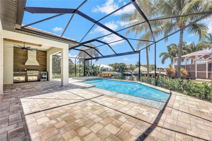 View of swimming pool with ceiling fan, a lanai, a patio area, a grill, and an outdoor kitchen