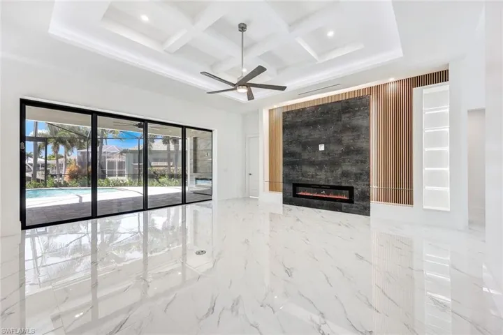 Unfurnished living room with a fireplace, beam ceiling, tile patterned floors, coffered ceiling, and ceiling fan