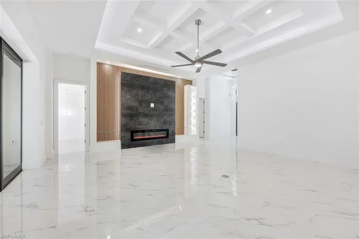 Unfurnished living room with light tile patterned flooring, a tile fireplace, beamed ceiling, coffered ceiling, and ceiling fan