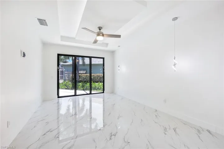Tiled empty room with ceiling fan and a tray ceiling