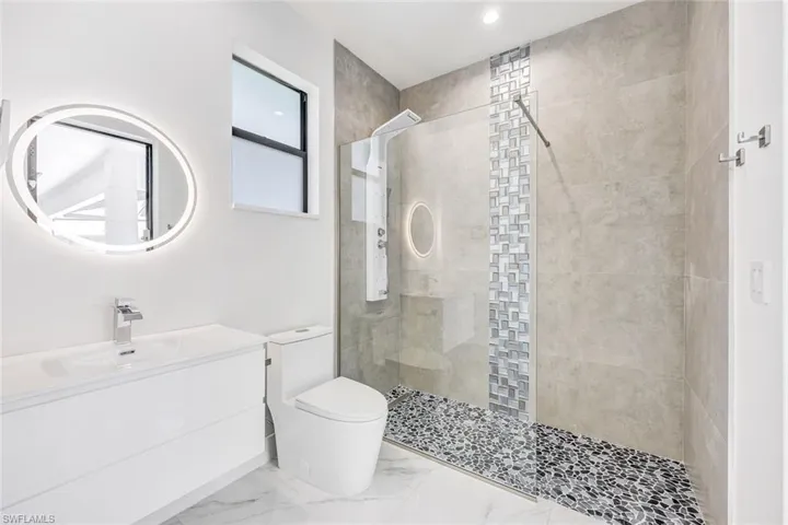 Bathroom featuring tile patterned flooring, vanity, tiled shower, and toilet