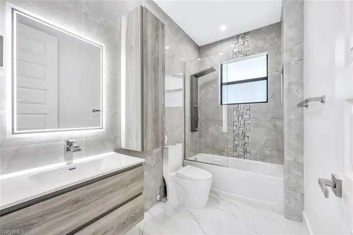 Full bathroom featuring combined bath / shower with glass door, vanity, tile patterned floors, tile walls, and toilet