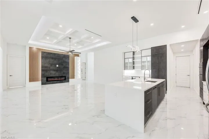 Kitchen featuring an island with sink, a tiled fireplace, coffered ceiling, ceiling fan, and light tile patterned floors