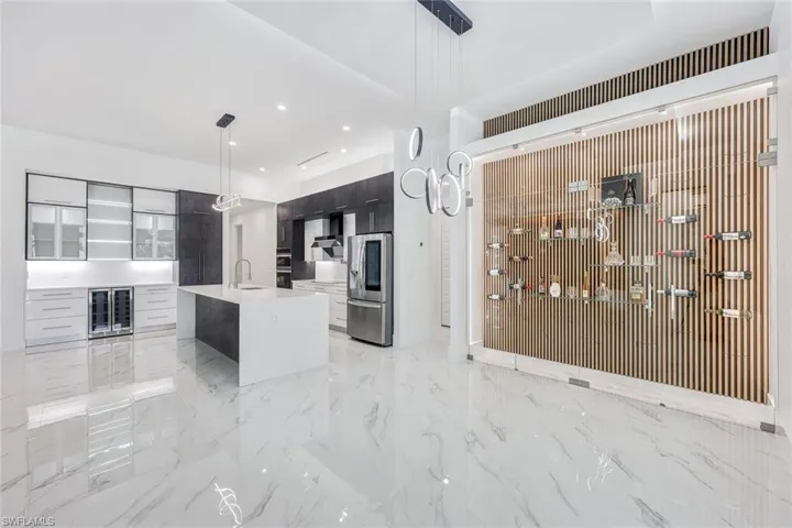Kitchen with stainless steel refrigerator with ice dispenser, an island with sink, light tile patterned floors, sink, and decorative light fixtures