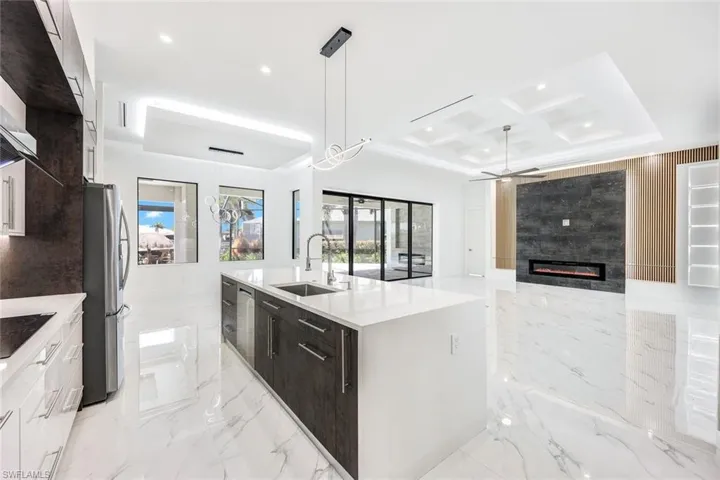 Kitchen with sink, a kitchen island with sink, coffered ceiling, stainless steel fridge, and hanging light fixtures