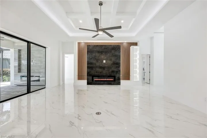 Unfurnished living room with ceiling fan, coffered ceiling, a large fireplace, and light tile patterned flooring