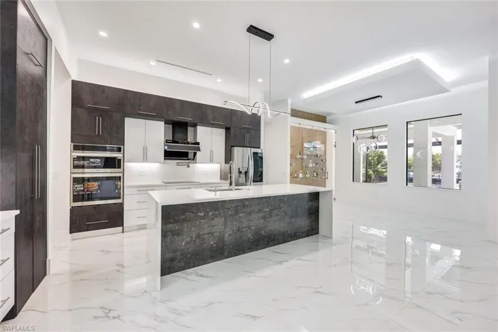 Kitchen with light tile patterned floors, appliances with stainless steel finishes, sink, and an island with sink