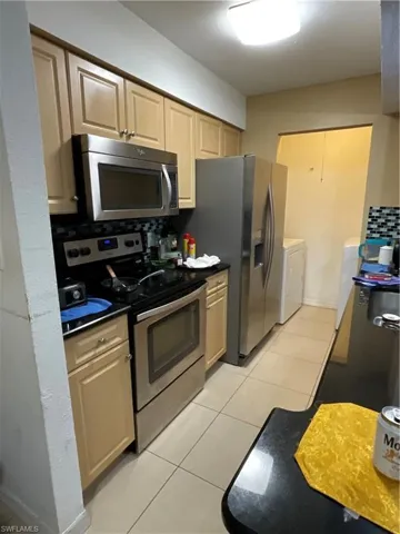 Kitchen featuring light brown cabinetry, tasteful backsplash, washer and dryer, stove, and light tile patterned floors