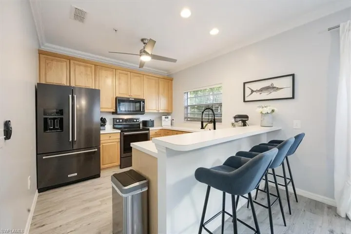 Kitchen with kitchen peninsula, stainless steel fridge, electric range, a breakfast bar area, and light hardwood / wood-style floors