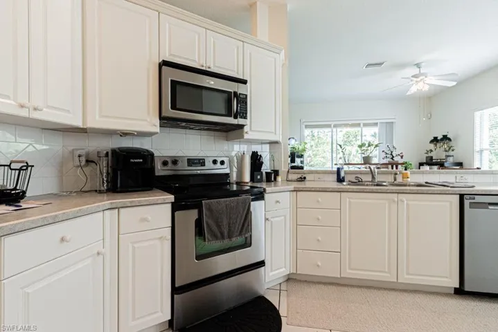 Kitchen featuring stainless steel appliances, a ceiling fan, decorative backsplash, and white cabinets