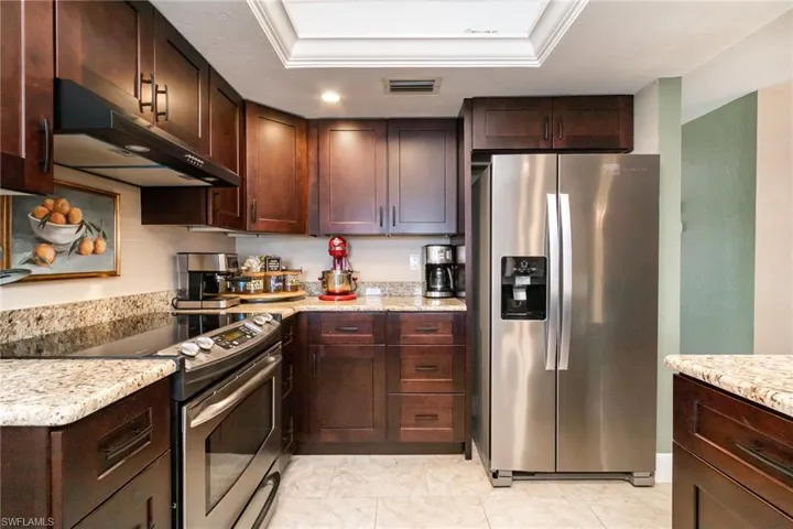 Kitchen featuring visible vents, a raised ceiling, appliances with stainless steel finishes, dark brown cabinetry, and under cabinet range hood