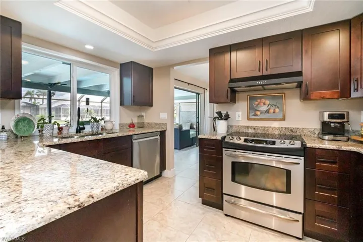 Kitchen with dark brown cabinetry, under cabinet range hood, a sink, and stainless steel appliances