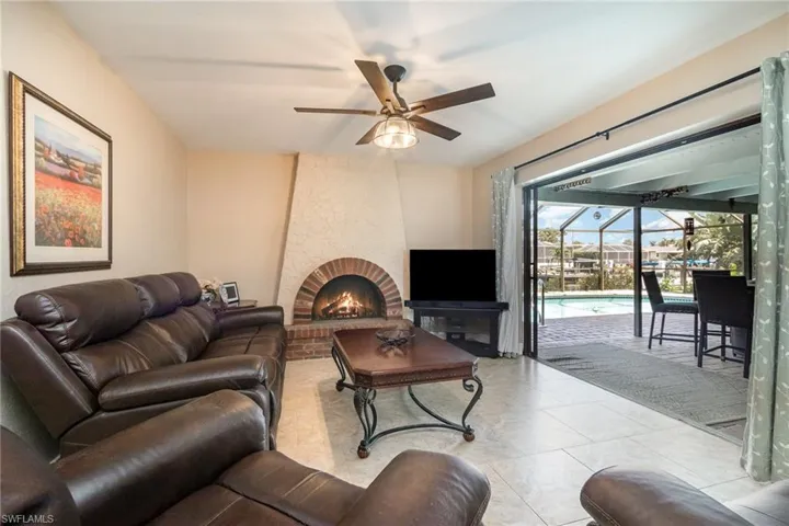 Living room featuring a sunroom, tile patterned floors, a ceiling fan, and a brick fireplace