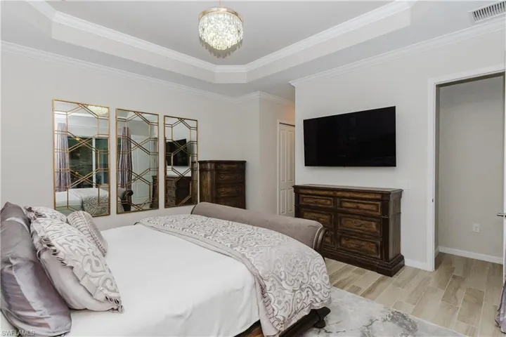 Tray ceiling with crown molding, crystal chandelier, and wood look tile flooring