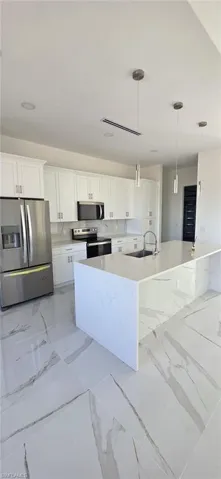 Kitchen featuring stainless steel appliances, white cabinets, decorative light fixtures, light stone countertops, and light marble finish flooring
