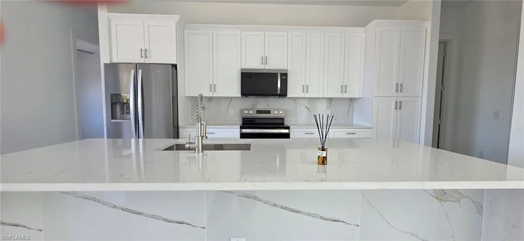 Kitchen featuring white cabinetry, stainless steel appliances, light stone countertops, and a large island with sink