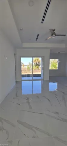 Unfurnished room with a raised ceiling, healthy amount of natural light, ceiling fan, and light marble finish flooring