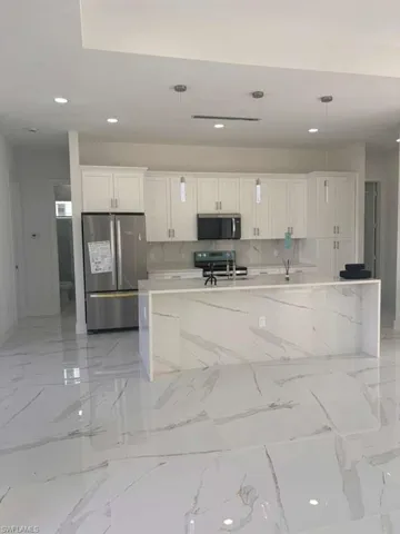 Kitchen with light stone counters, white cabinetry, stainless steel appliances, a spacious island, and pendant lighting