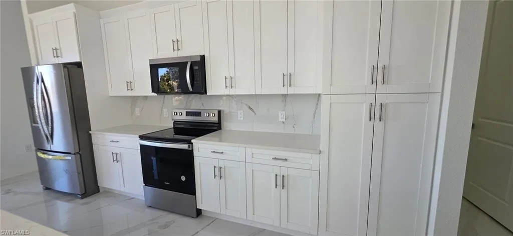 Kitchen featuring stainless steel appliances, white cabinetry, light marble finish floors, decorative backsplash, and light stone counters