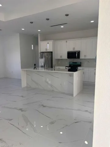Kitchen featuring a center island with sink, stainless steel appliances, white cabinetry, light stone counters, and decorative light fixtures