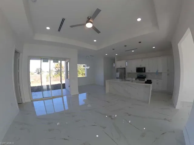 Unfurnished living room featuring ceiling fan, a raised ceiling, recessed lighting, and light marble finish floors