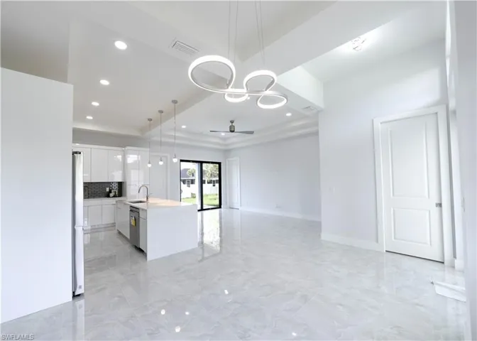 Kitchen with a kitchen island with sink, hanging light fixtures, white cabinetry, appliances with stainless steel finishes, and ceiling fan