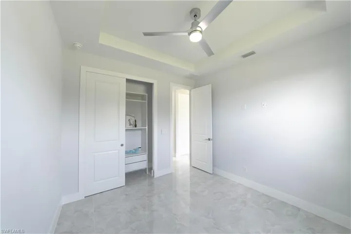 Unfurnished bedroom with a closet, a tray ceiling, and ceiling fan