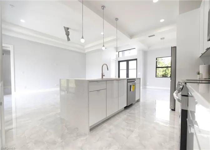 Kitchen featuring a center island with sink, sink, white cabinets, decorative light fixtures, and appliances with stainless steel finishes