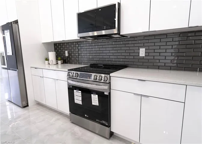 Kitchen with appliances with stainless steel finishes, white cabinets, and tasteful backsplash