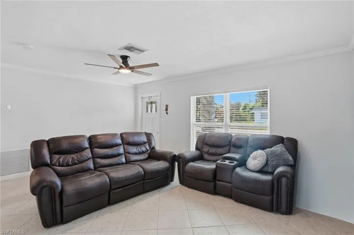 Living room featuring ornamental molding, light tile patterned flooring, and a ceiling fan