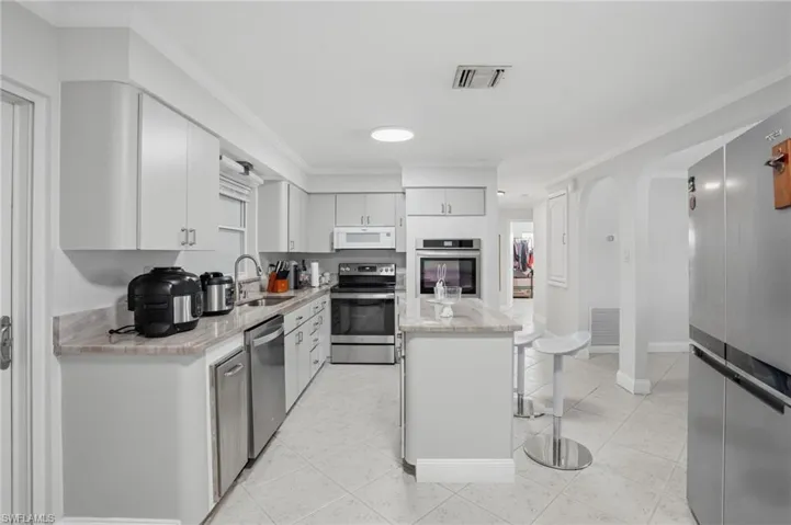 Kitchen featuring a breakfast bar, stainless steel appliances, ornamental molding, a kitchen island, and light stone countertops