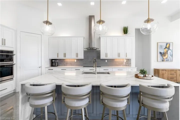 Kitchen featuring wall chimney exhaust hood, white cabinetry, and hanging light fixtures