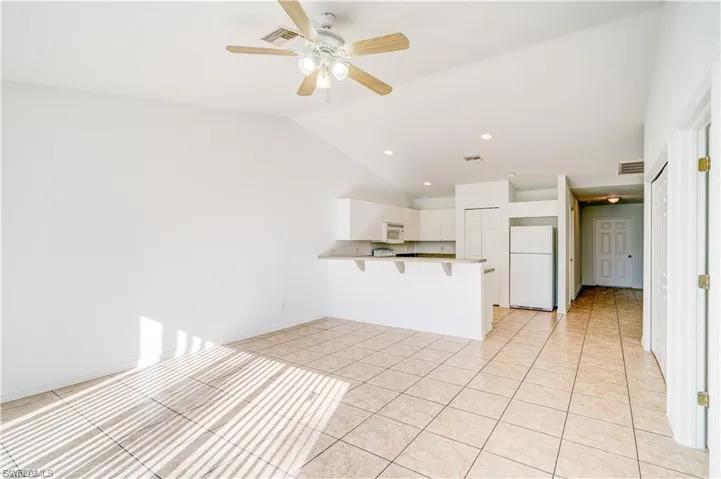 Kitchen featuring white appliances, a peninsula, a kitchen breakfast bar, vaulted ceiling, and ceiling fan