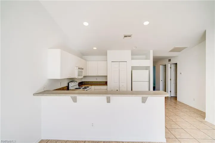 Kitchen featuring a kitchen bar, a peninsula, white appliances, white cabinets, and light tile patterned floors