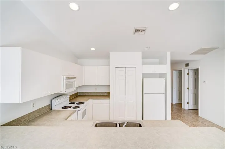 Kitchen featuring white appliances, light countertops, white cabinetry, recessed lighting, and light tile patterned flooring